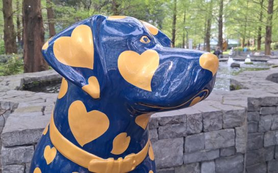 A statue of a dog in Canary Wharf's Jubilee Park. The statue is painted dark blue and decorated with gold hearts.