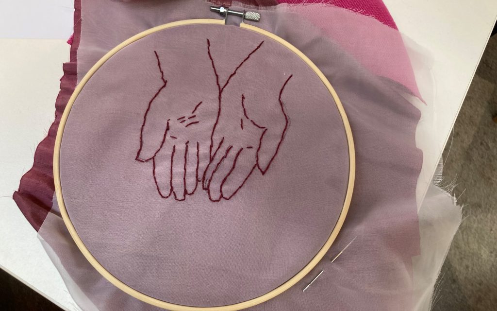 Hand embroidery of a pair of outstretched hands.