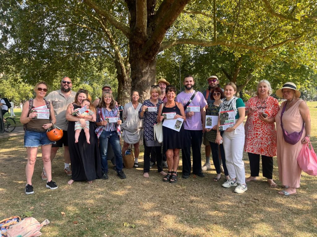 A large group of people holding campaign literature on a sunny day in a park