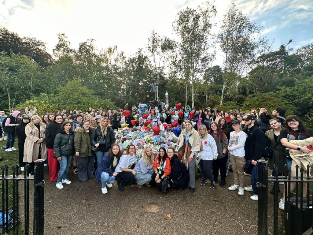 Organisers and fans pose for a photo at the memorial, where the Peter Pan statue is covered with flowers, letters and balloons.